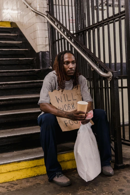 a man sitting down with a bag and a sign