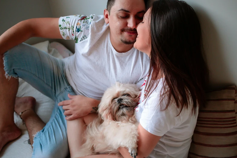 a young couple cuddles in bed while their dog holds the puppy