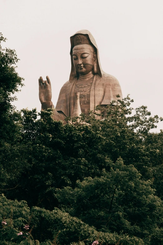 large buddha statue sitting above shrubbery with a bird perched on the top