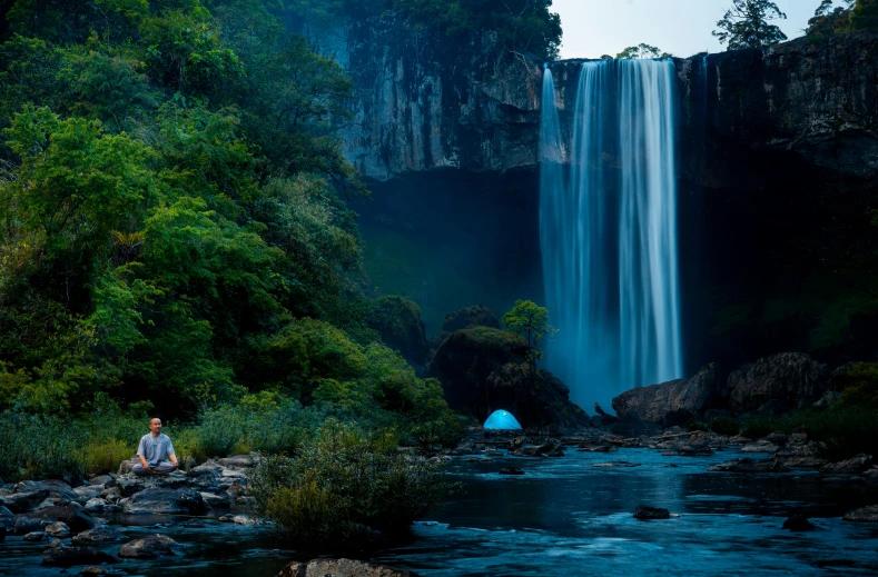 a man sitting near a waterfall watching the river