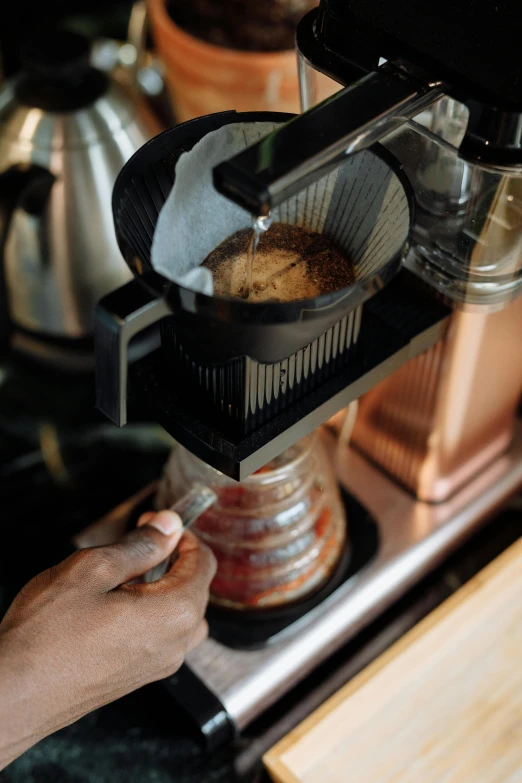 the person is holding the cup on the coffee maker