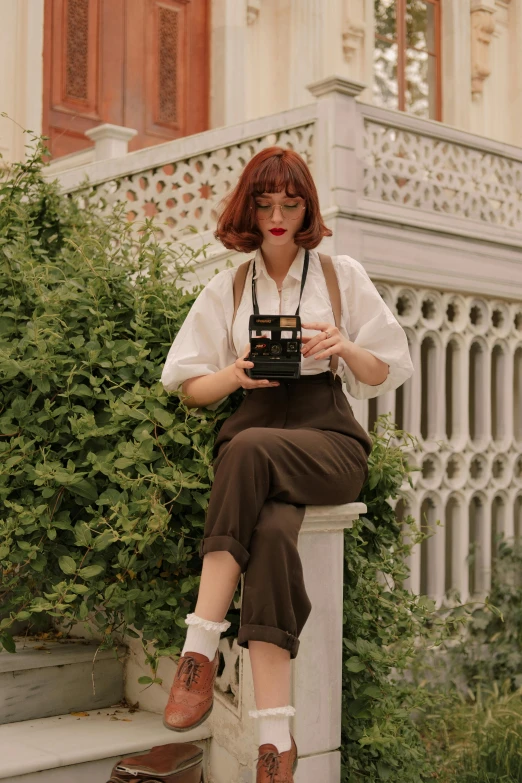 a young woman in overalls and suspenders is holding an old camera