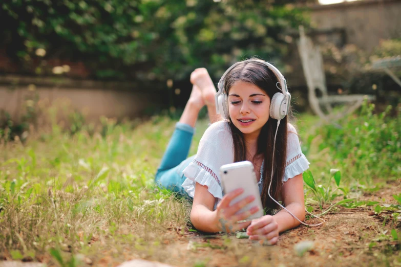 a woman sitting on grass with headphones and using an mp3 player