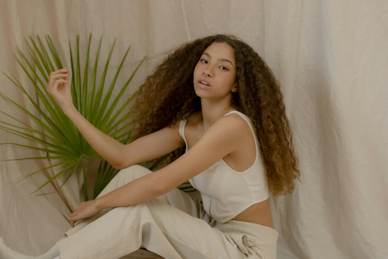 woman posing in white clothing holding plant sitting on a wooden floor