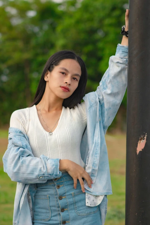 a young woman leaning against a pole in a park