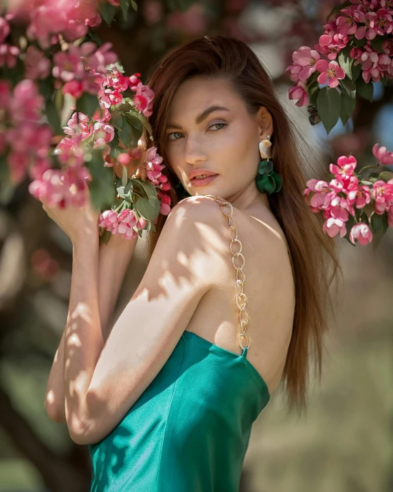 the beautiful brunette girl is standing near a blossomy tree