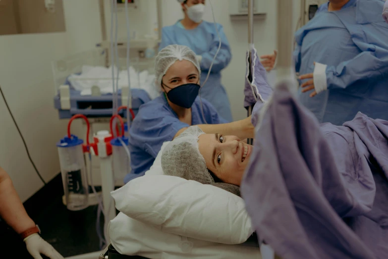 a woman lying down while some nurses stand behind her