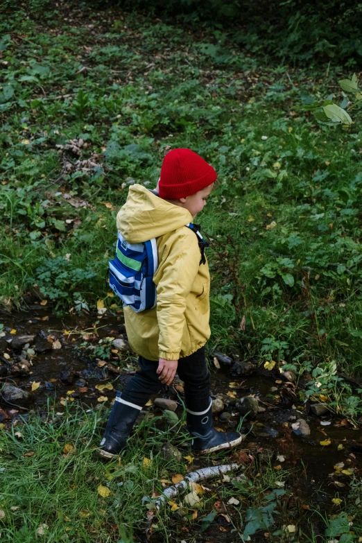 a small  wearing a yellow jacket is carrying a skateboard