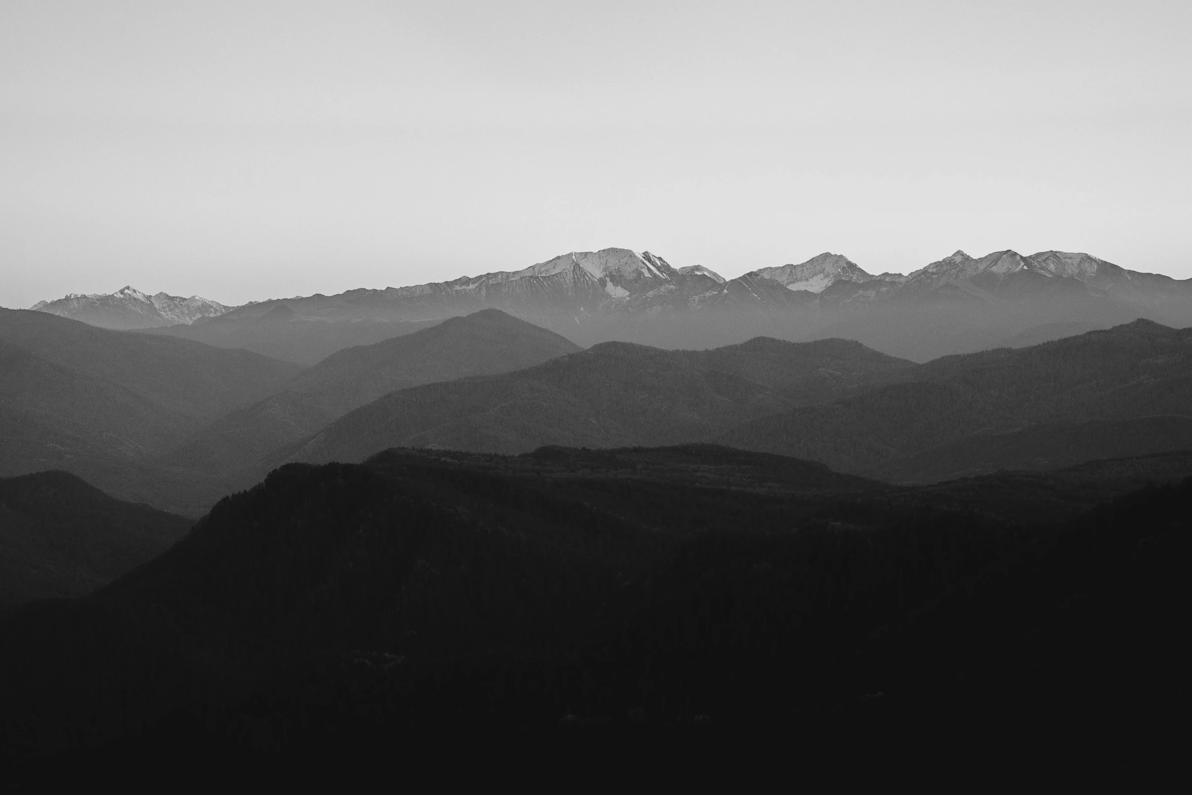 the peak of a mountain range is silhouetted against the grey sky