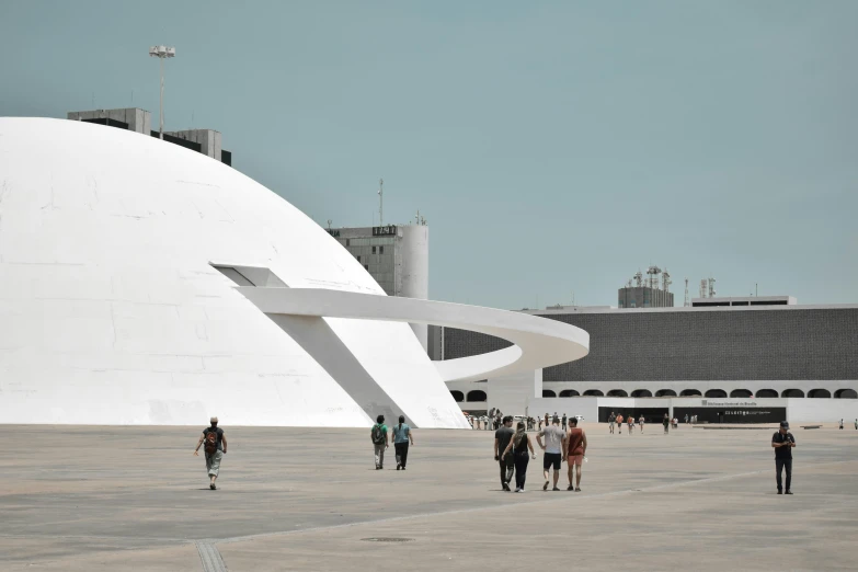 people walking around outside a building, while a plane flies by