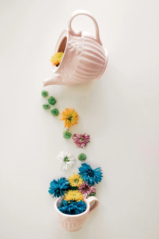 a watering can full of small flowers sitting next to another cup of flowers