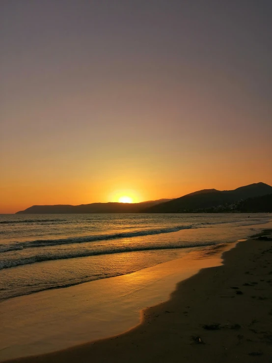 there is a lone surfboard on the beach at sunset