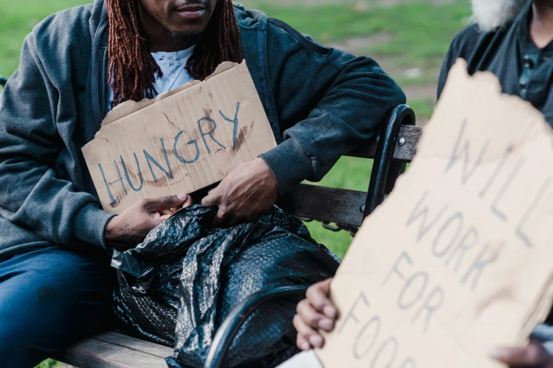 a man sitting on top of a wooden bench holding a sign