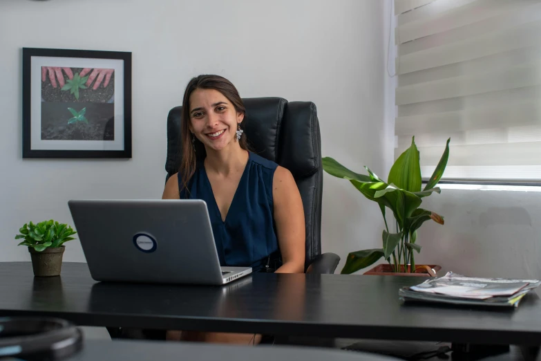 a woman smiles in a chair with her laptop on her desk