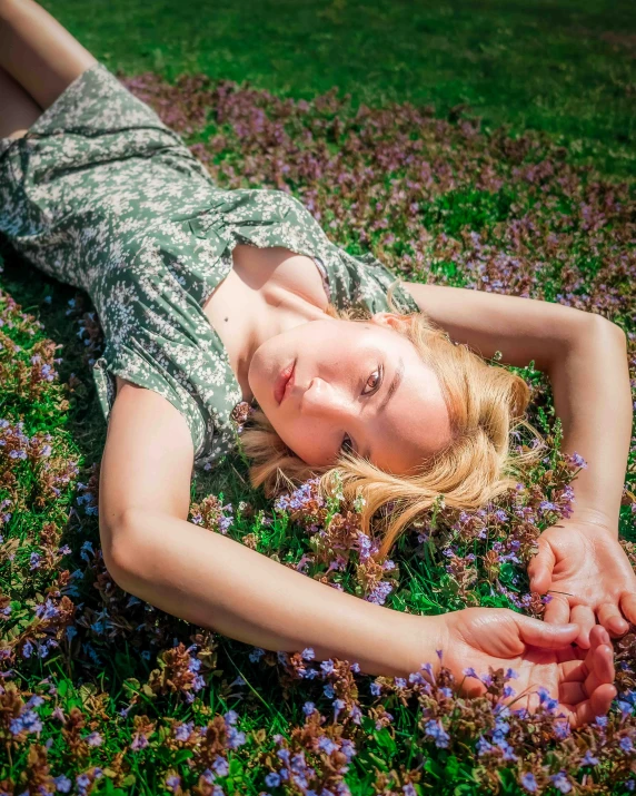 a pretty woman laying on top of a lush green field