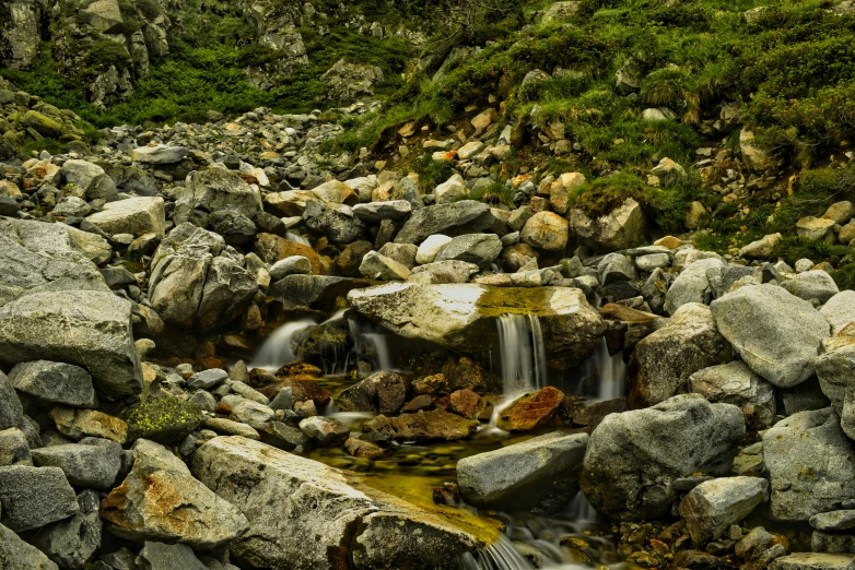 a stream of water surrounded by rocks and green grass