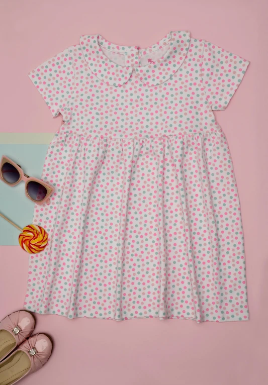 pink and white dress on a table next to sunglasses and lollipop