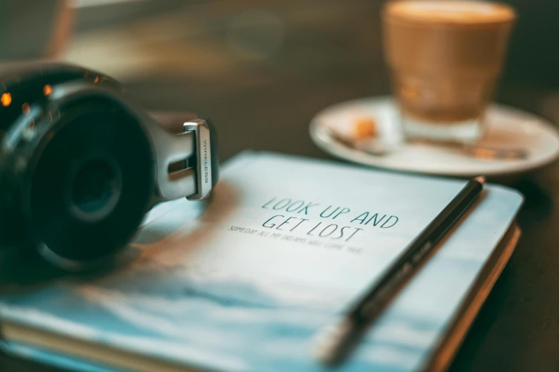 a po of a book and pen on a table with two coffee mugs