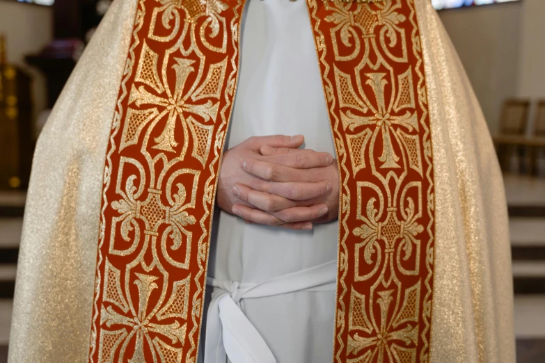 closeup of the hands of a priest wearing an orange stole