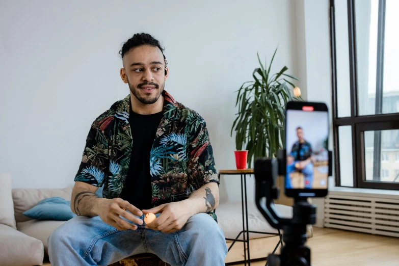 man wearing hawaiian shirt and jeans in living room with camera