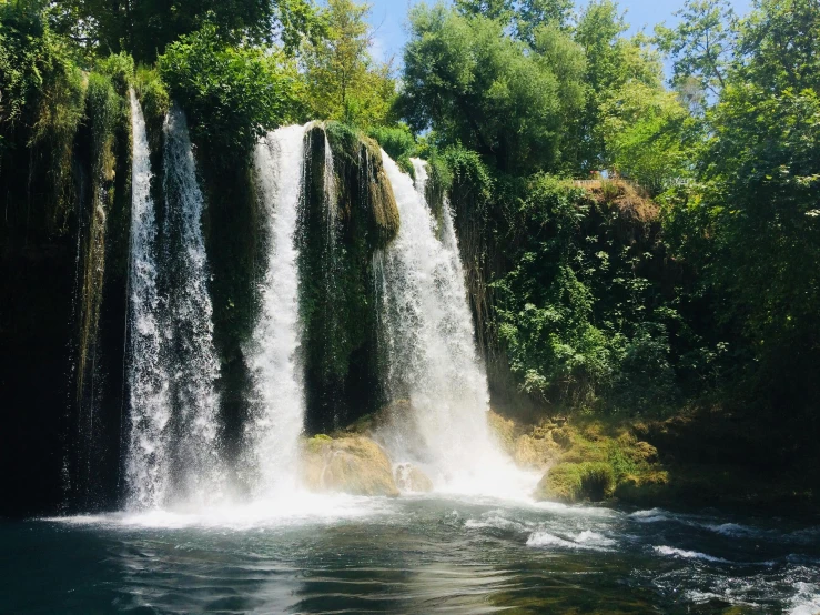 people swimming at a lake by some very tall waterfalls