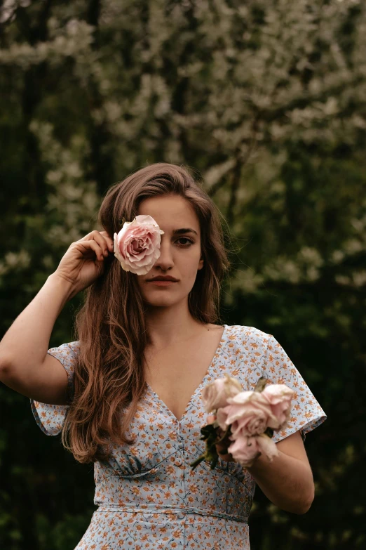 a woman is holding two pink flowers to her ear