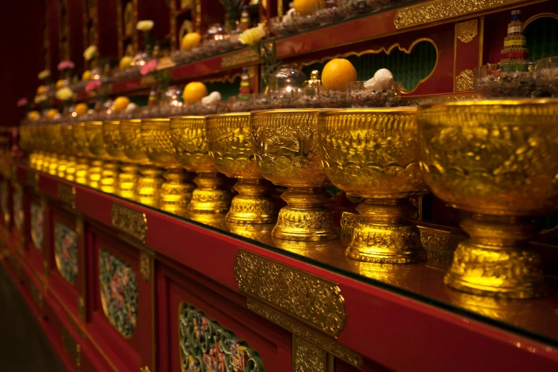 a row of shiny golden bowls line the shelves of a large room