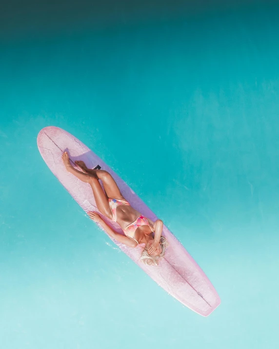 an overhead view of a young woman on a pink surfboard