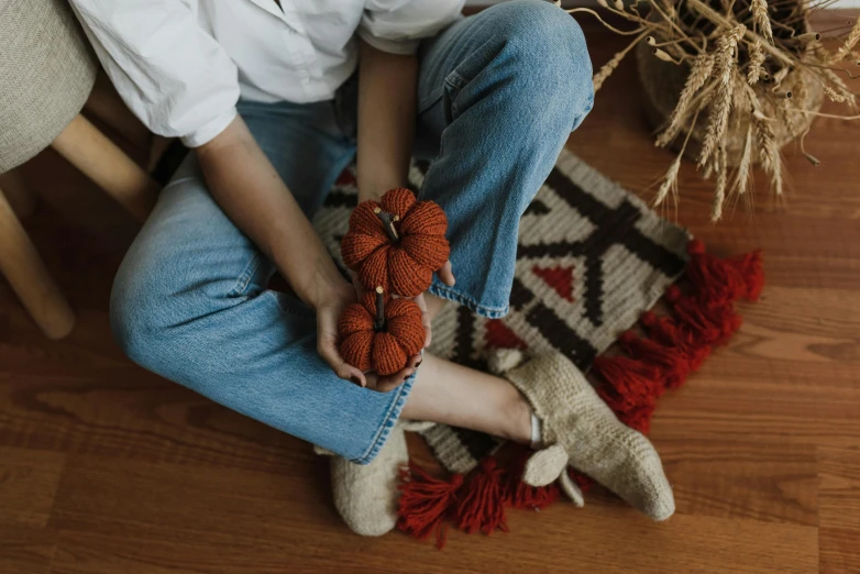 a woman sits on the floor and holds two pieces of knitted items