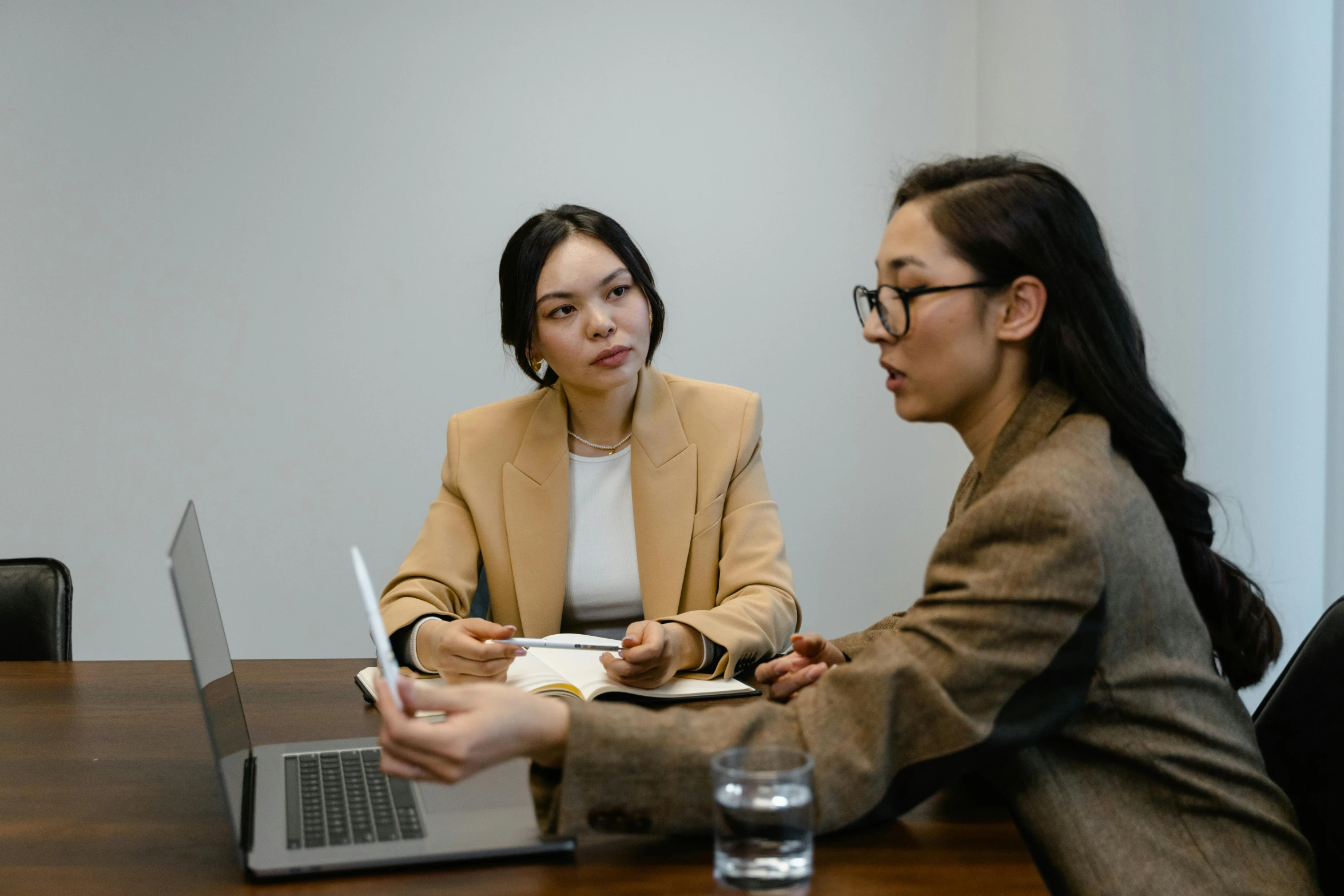 two women are sitting at a table and looking at a laptop