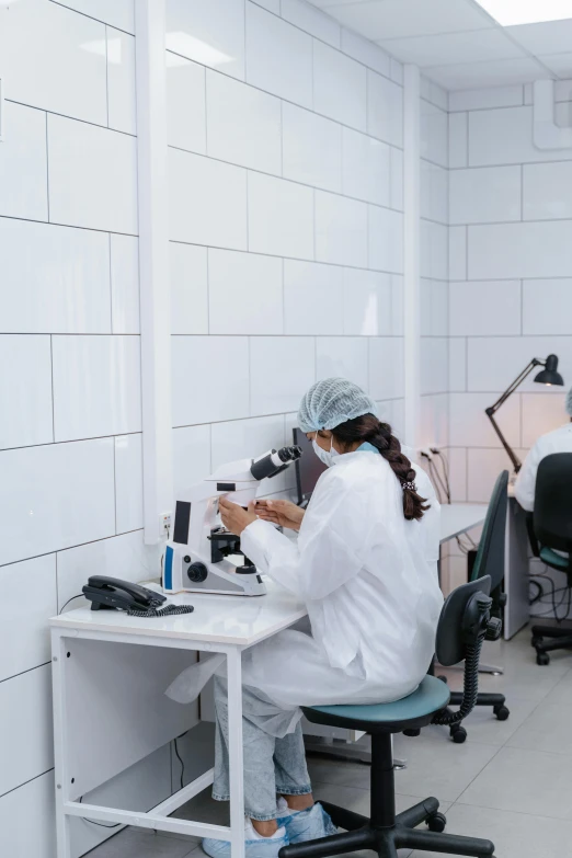 a woman sits at a desk while looking through microscopes