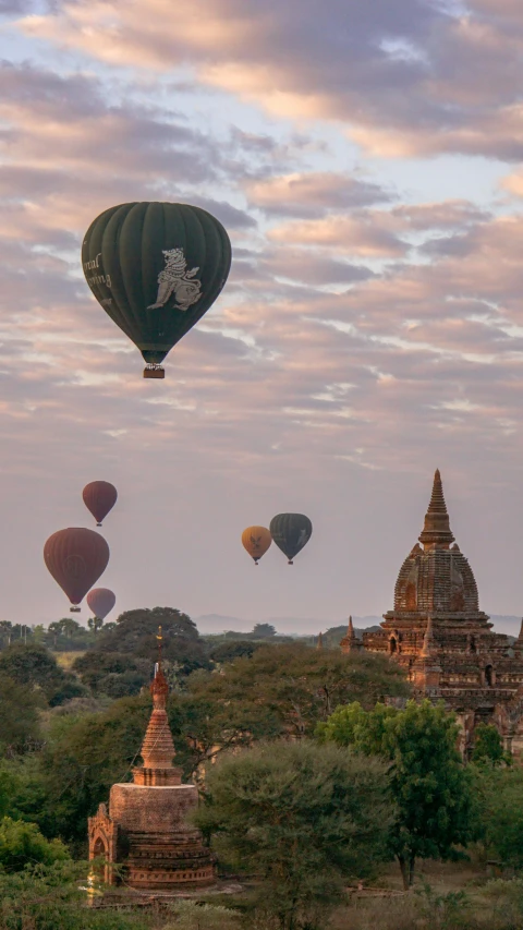 several  air balloons flying over an ancient looking building