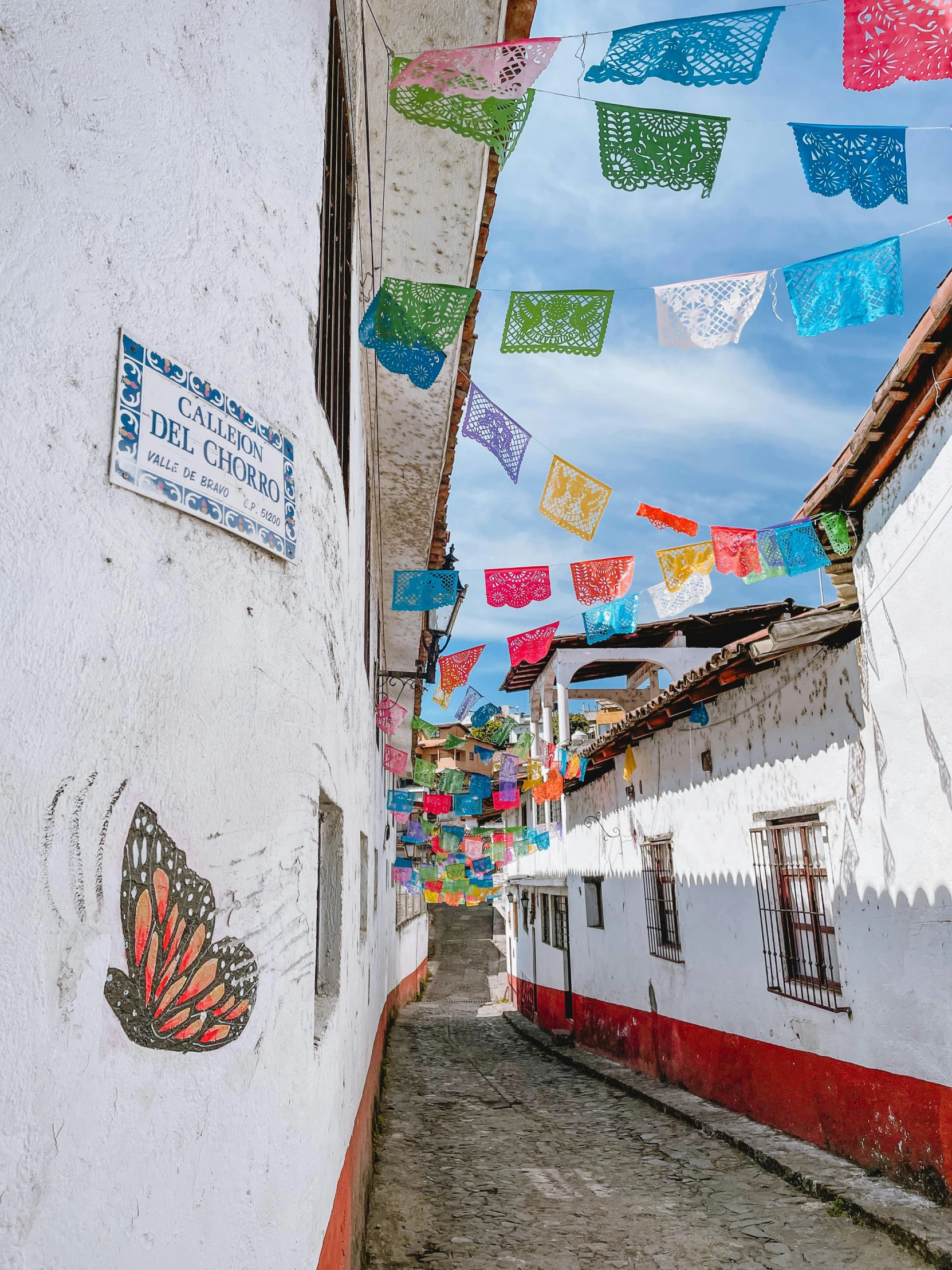 colorful flags hung over narrow white buildings with a sky background