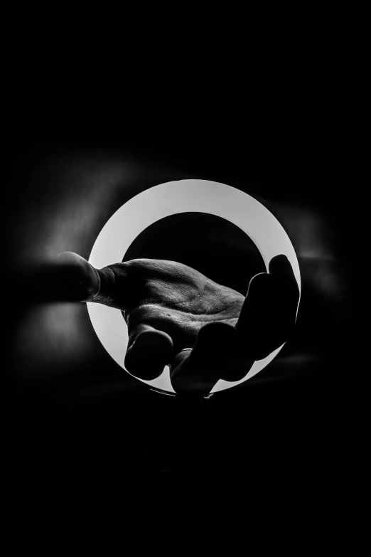 silhouetted hand holding a black object with white circle behind it