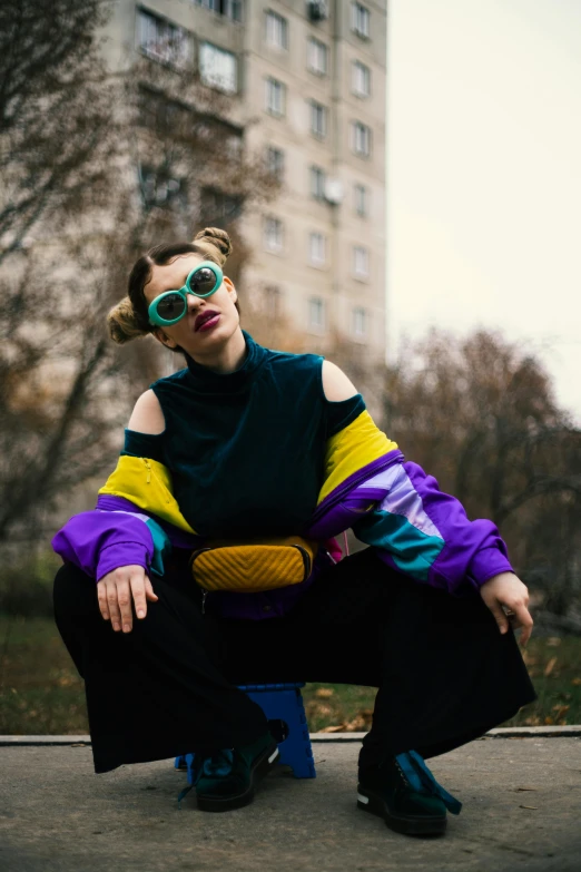 a young woman poses in front of a building wearing sunglasses