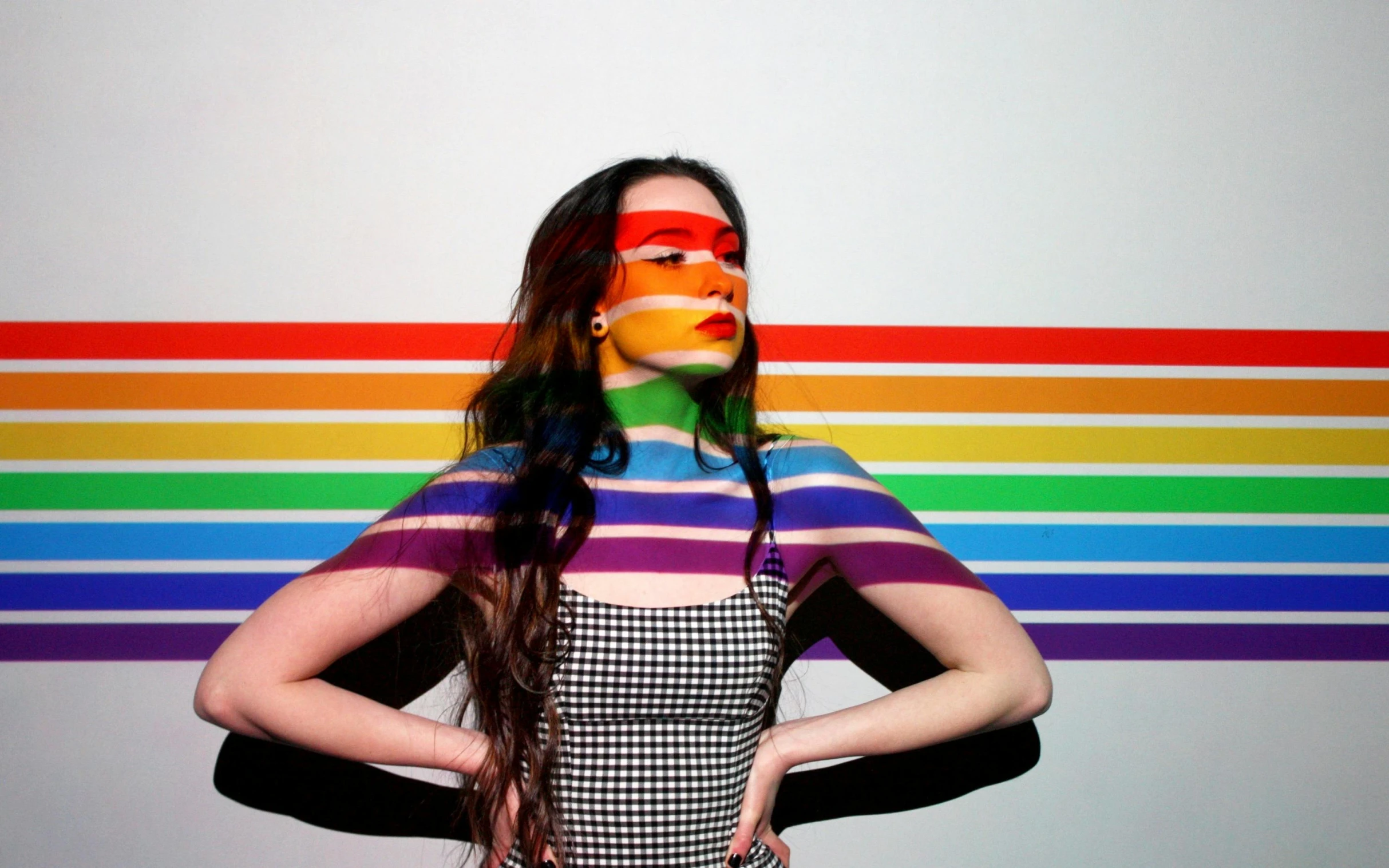a young woman has her hands in her hair as she looks down as the background is colored by rainbow