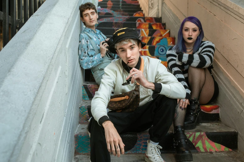 a boy smoking his cigarette while two other young people watch him on the stairs