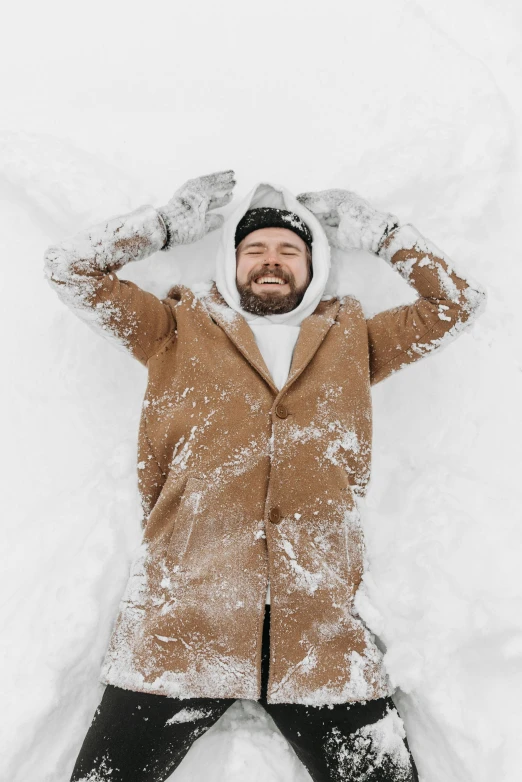 a man laying in snow while wearing a coat