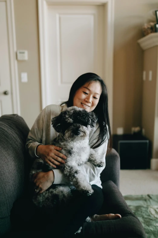 a woman sits on the couch holding her dog