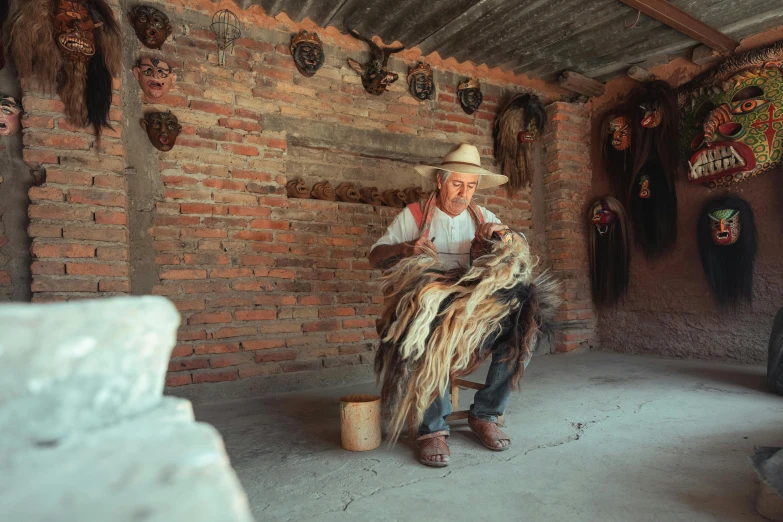 the man sits on a stool with his foot on a bucket holding a piece of fur