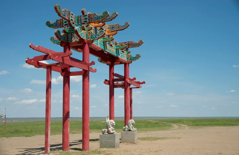 red wooden statues are on a dirt road near green grass