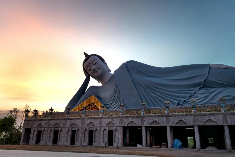 large statue of woman with blue shawl in front of a sun set