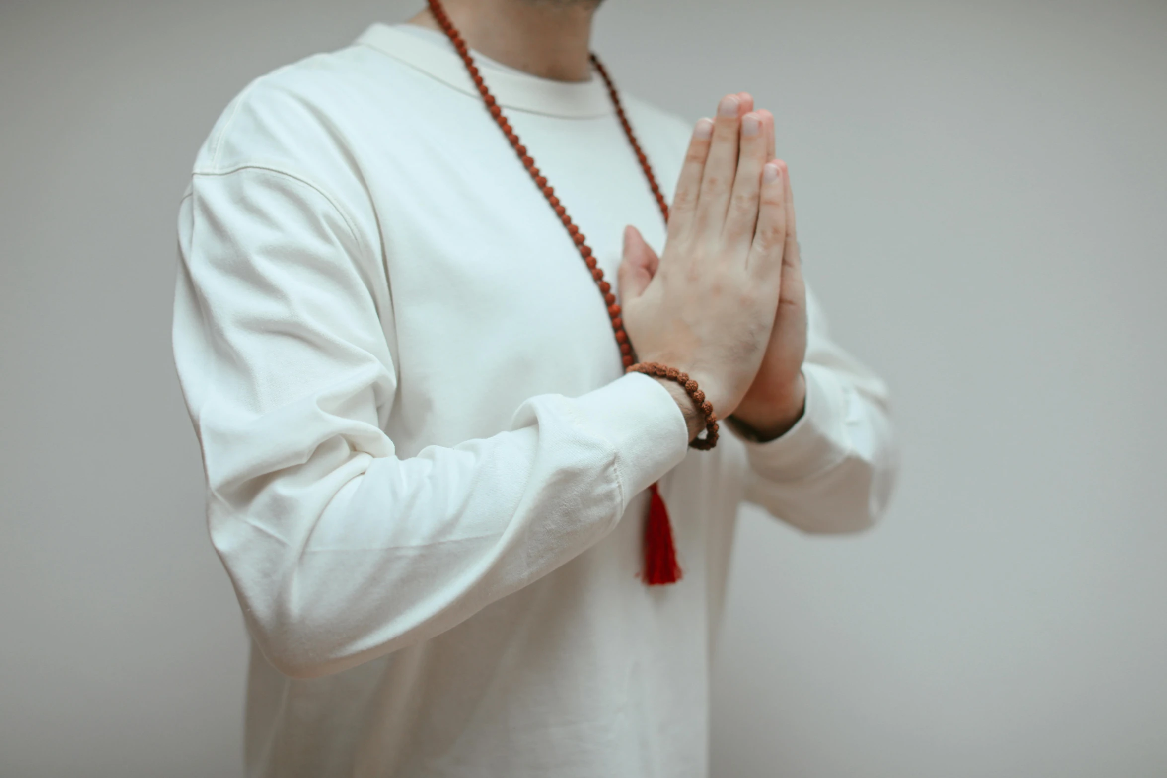 a man wearing a red necklace and holding his hands together