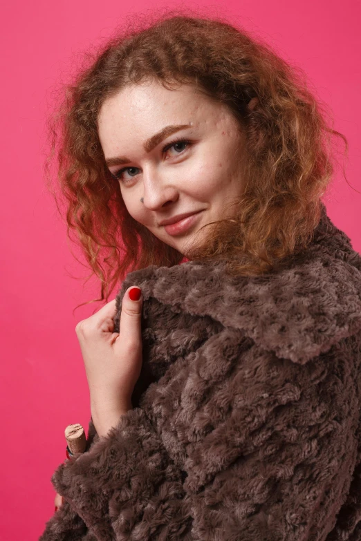 a woman with red hair and blue eyes is standing near a pink background