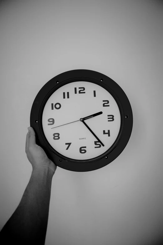 a hand holds up an analog clock on a wall