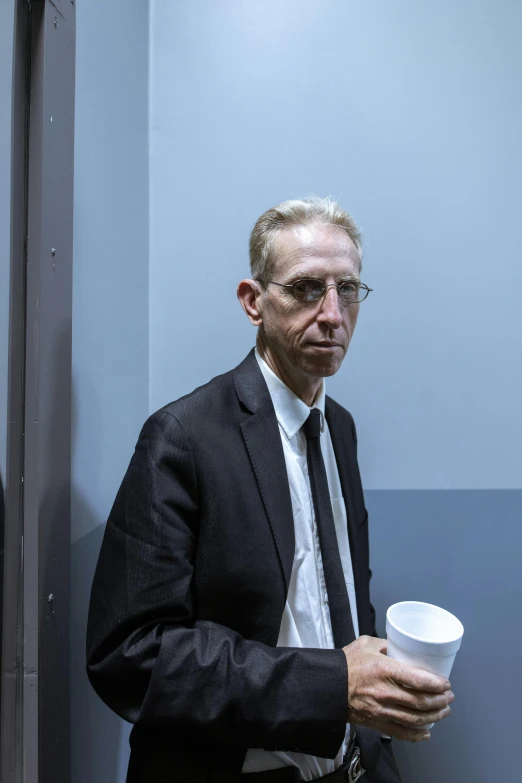 man in business suit standing at a mirror drinking a cup of coffee