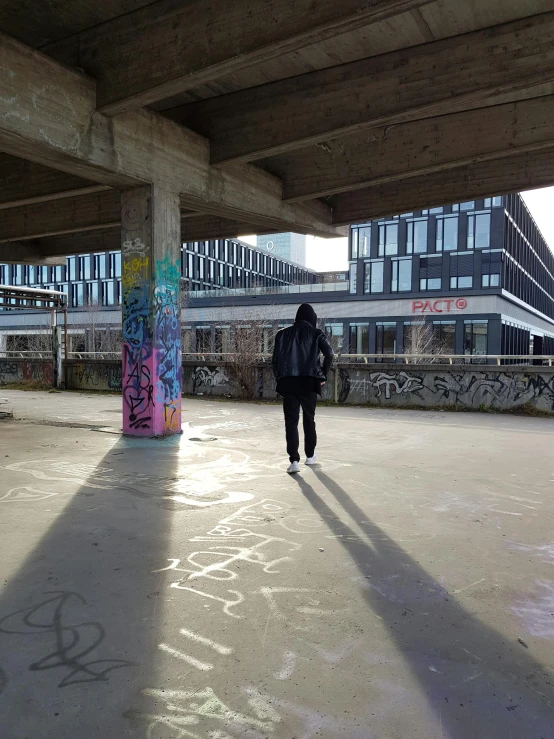 a man walking under a bridge with a skateboard under his feet