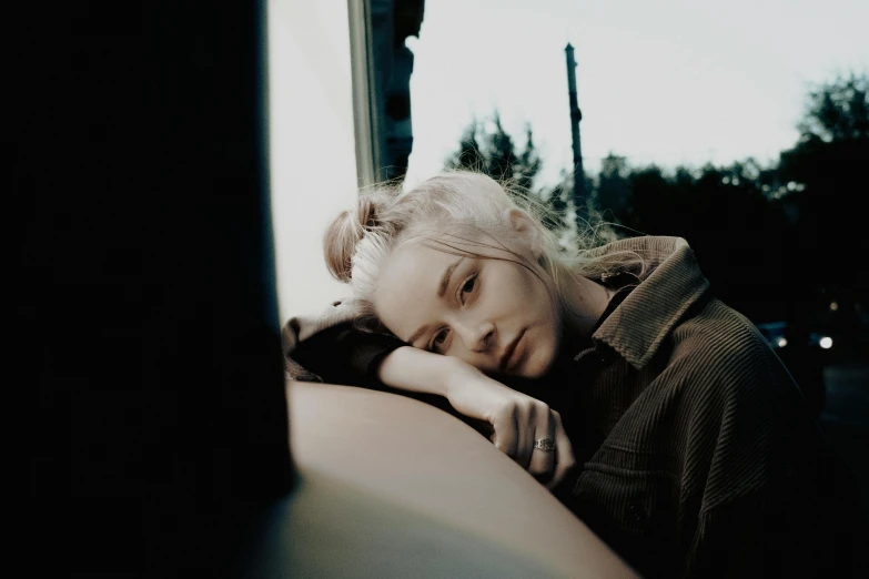 a woman sitting down next to a window in the evening