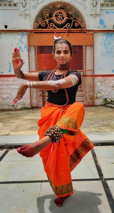 a woman with orange colored sari performing an indian dance