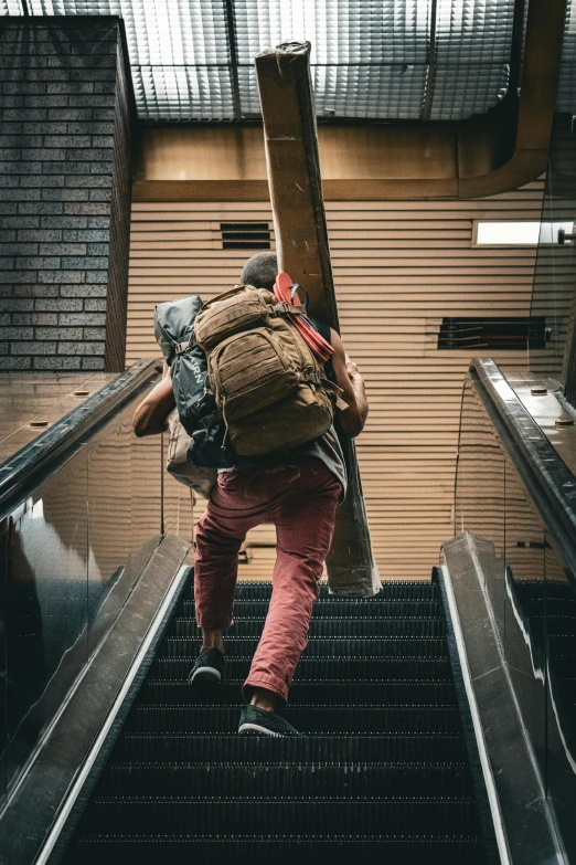 man wearing backpack ascending an escalator with backpacks on back